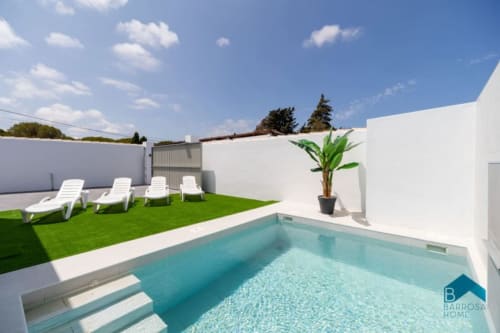Piscina y jardín de Barrosa Home con tumbonas, césped artificial y muros blancos modernos bajo cielo azul