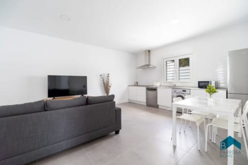 Espacio de vivienda abierto y moderno en Barrosa Home con sofá gris, televisor, comedor y cocina equipada