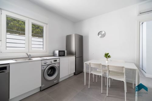 Cocina moderna en Barrosa Home con muebles blancos, refrigerador acero inoxidable, lavadora y mesa de comedor