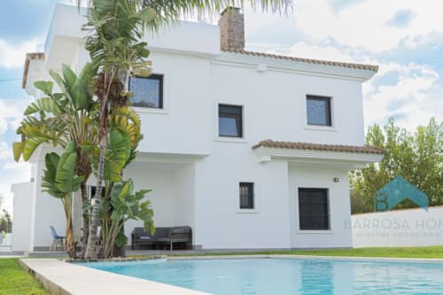 Villa moderna blanca con piscina, palmeras y zona de estar en Barrosa Home, alquiler vacacional en España