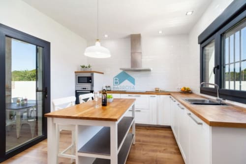 Cocina moderna en Barrosa Home con encimeras de madera, muebles blancos, isla central y amplios ventanales con vistas al paisaje