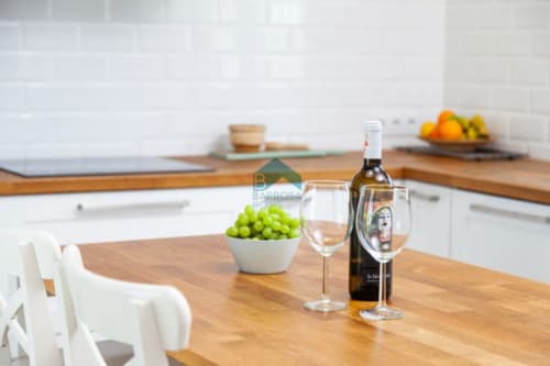 Área de comedor de la cocina Barrosa Home con mesa de madera, botella de vino, uvas y sillas blancas