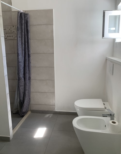 Bagno moderno in Ca' Salino B&B con bidet e wc bianchi, doccia con box in vetro e tenda grigia, lavandino, specchio e