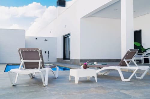 Moderner Poolbereich im Barrosa Home mit weißen Sonnenliegen, braunen Kissen und blauem Swimmingpool