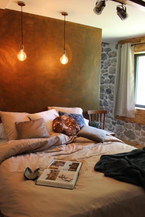 Chambre cosy au Petit Bégou avec mur d'accent couleur rouille, luminaires suspendus et vue sur le jardin près de Saint-Auban-d'Oze