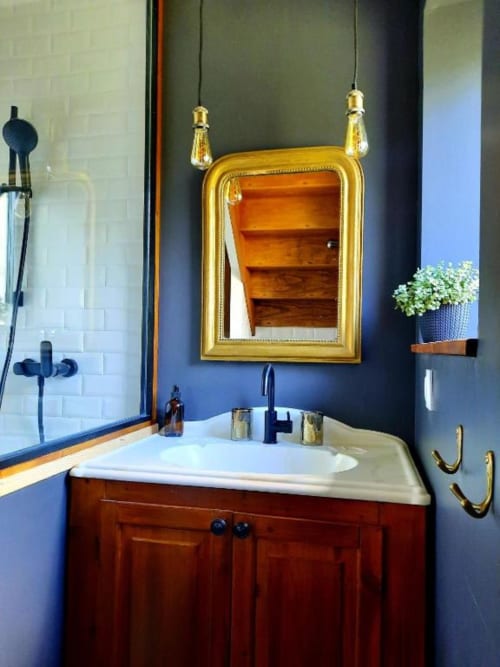 Salle de bains élégante au Petit Bégou : miroir doré, murs bleu foncé, vanité en bois et accessoires en laiton