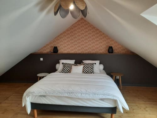 Chambre mansardée moderne au Petit Bégou : lit blanc, tête de lit noire, papier peint motifs, parquet et suspension