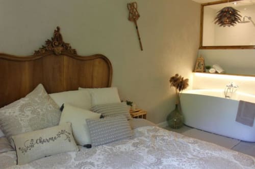 Élégante chambre au Petit Bégou avec tête de lit sculptée, literie blanche et baignoire dans la salle de bain attenante.