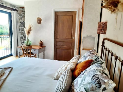 Chambre douillette au Petit Bégou avec lit, bureau en bois, mur en pierre et balcon avec vue sur le jardin à Saint-Auban-d'Oze