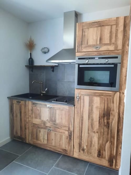 Kitchenette moderne aux armoires en bois, plan de travail noir, cuisinière en acier inoxydable et hotte aspirante à l'appartement Le Petit Bégou
