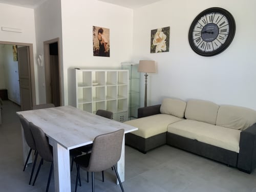Ampia zona living dell'appartamento Terra a Ca' Salino con tavolo da pranzo, divano color crema, mobile contenitore e orologio con vista giardino