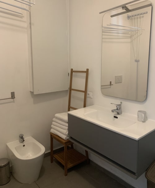 Bagno moderno dell'appartamento Terra a Ca' Salino con lavabo, bidet, WC, specchio e asciugamani bianchi su scala in legno