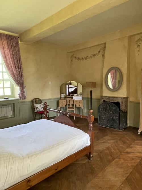 Chambre Gîte Voltaire du Château de la Motte avec lit en bois, miroir de coiffeuse, cheminée et mobilier d'époque