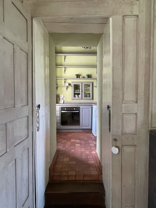 Couloir menant à la cuisine du Gîte Voltaire au Château de la Motte, Joué-du-Plain, avec carrelage en terre cuite et portes crème
