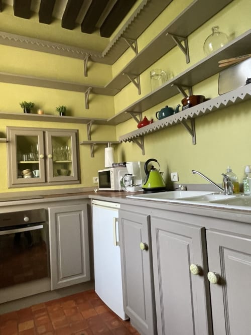 Cuisine jaune éclatant à la Gîte Voltaire du Château de la Motte, avec meubles blancs, étagères ouvertes et bouilloire verte