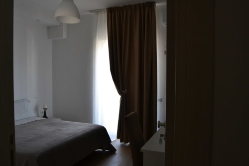 Camera da letto Makasa B&B a Villapiana con letto, tende marroni, lampada a sospensione e luce naturale dalla porta-finestra del balcone