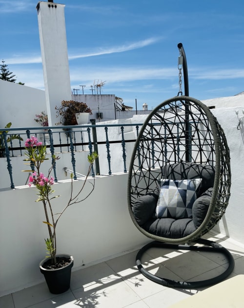 Woven egg chair with cushions on terrace at Victoria Seis apartment, Medina Sidonia, with flowering plants and white-washed