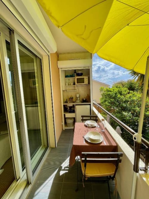 Hotel l'Orangeraie balcony with yellow sunshade, dining table, and garden views in Le Lavandou