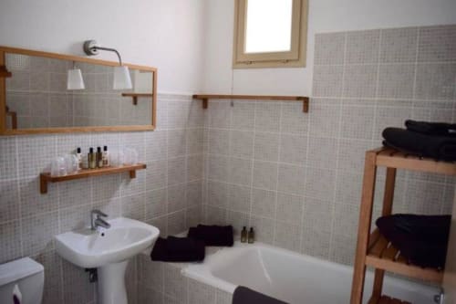Modern bathroom in Hôtel l'Orangeraie Lavandou villa with tiled walls, white sink, bathtub, and wooden shelving with