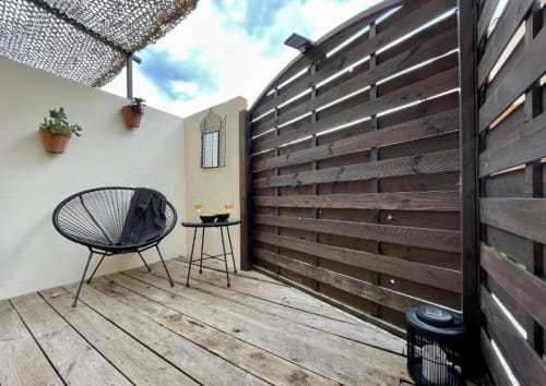 Modern patio terrace at Hôtel l'Orangeraie Lavandou with black lounge chair, dark wooden privacy screens, potted plants, and