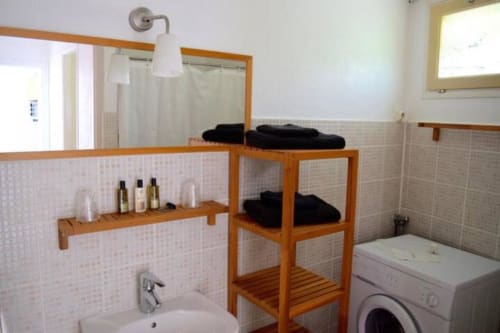 Bathroom at Hôtel l'Orangeraie Lavandou villa with wooden shelving, sink, mirror, washing machine, and shower area