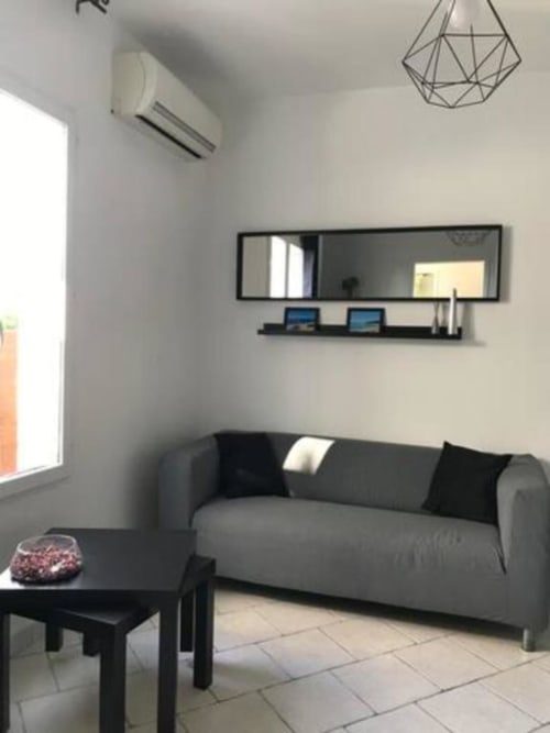 Modern living room at Hôtel l'Orangeraie Lavandou with gray sofa, black coffee table, wall mirror, and AC unit