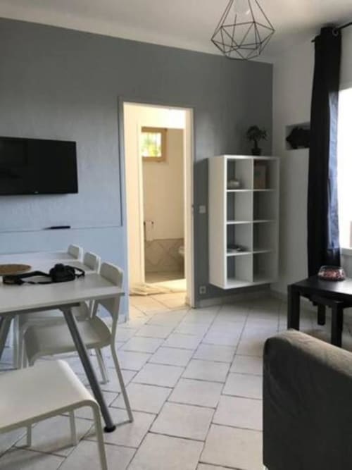 Modern villa living area with dining table, white shelving, flat-screen TV, and kitchen access at Hôtel l'Orangeraie Lavandou