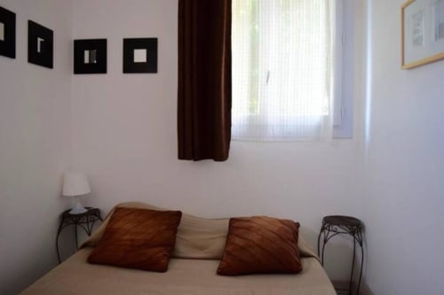Cozy bedroom with cream bed, burgundy pillows, dark curtains, and framed wall art in villa at Hôtel l'Orangeraie Lavandou