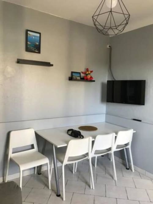 Modern villa dining area with white chairs, flat-screen TV, and geometric pendant light at Hôtel l'Orangeraie Lavandou