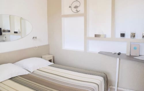 Bright, minimalist single room at Hôtel l'Orangeraie Lavandou with white bedding, desk, round mirror, and garden views