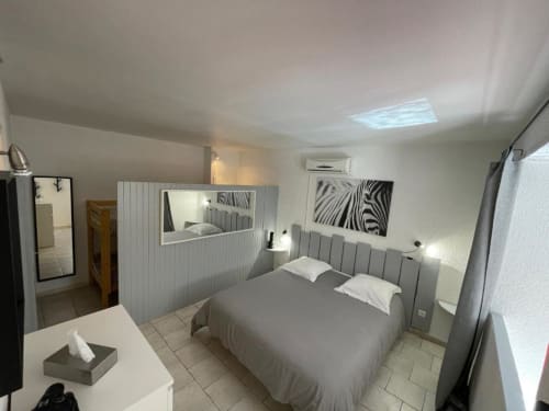 Chambre moderne de l'Hôtel l'Orangeraie Lavandou avec lit gris, murs blancs et art zèbre