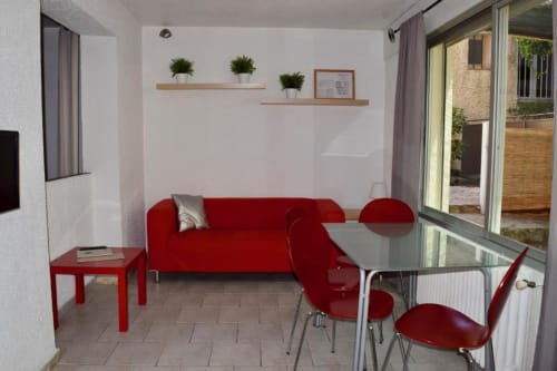 Élégant salon de l'Hôtel l'Orangeraie avec canapé rouge, table à manger et vue sur le jardin au Lavandou