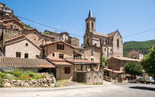 Historic stone village of Millau with church tower, traditional architecture, and green hillside backdrop