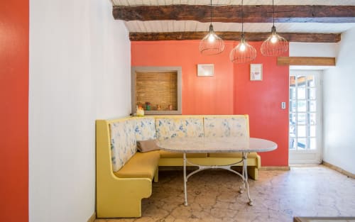 Modern lounge area with yellow banquette seating, coral walls, exposed beams, and pendant lighting in Dourbie Cottage, Millau
