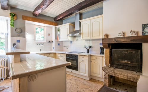 Rustic kitchen in Dourbie Cottage, Millau, with cream cabinets, exposed beams, fireplace, and countryside charm