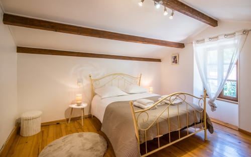 Cozy bedroom in Dourbie Cottage, Millau with ornate brass bed, wooden beams, hardwood floors and mountain views