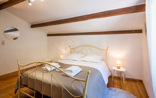 Bright bedroom with brass bed, white linens, exposed wooden beams, and warm lighting at Dourbie Cottage in Millau