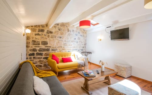 Cozy living room in Dourbie Cottage, Millau with yellow sofa, stone wall, wooden table and TV