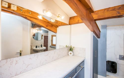 Modern bathroom in Dourbie Cottage, Millau with marble vanity, wooden beams, and large mirror