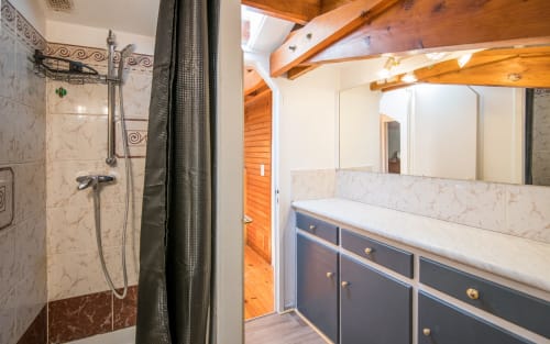 Modern bathroom in Dourbie Cottage with marble tile shower, dark vanity with white countertop, exposed wooden beams, and