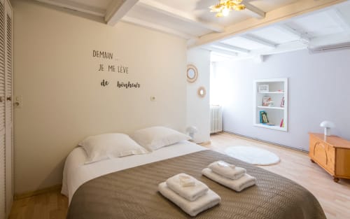 Bright bedroom in Dourbie Cottage, Millau with bed, white pillows, wooden furniture, bookshelf, and French wall text