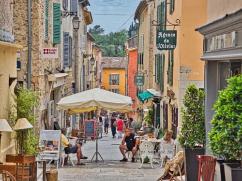 Charming medieval street in Spéracèdes with colorful buildings, outdoor café seating, and local shops