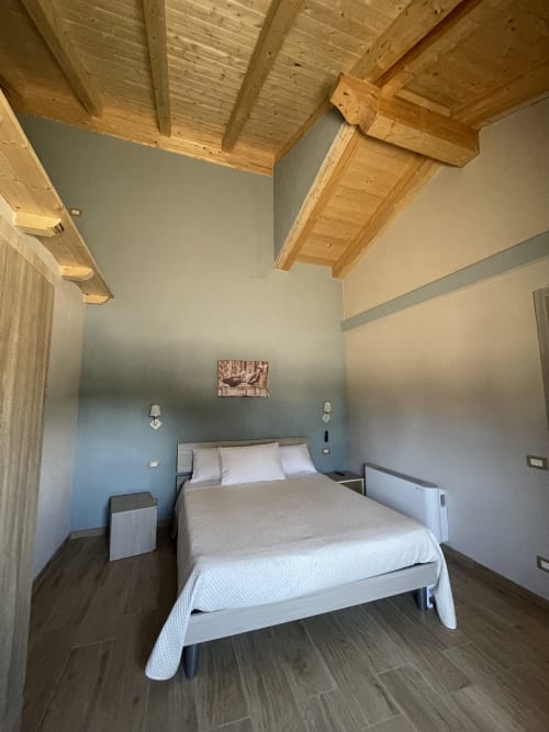 Camera moderna a Villa Maria con travi in legno, parete azzurra, letto queen e pavimento scuro nella Calabria rurale