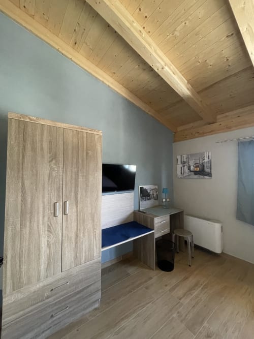 Camera moderna a Villa Maria con travi in legno, armadio, letto, scrivania, TV e vista sulla campagna di Cosenza