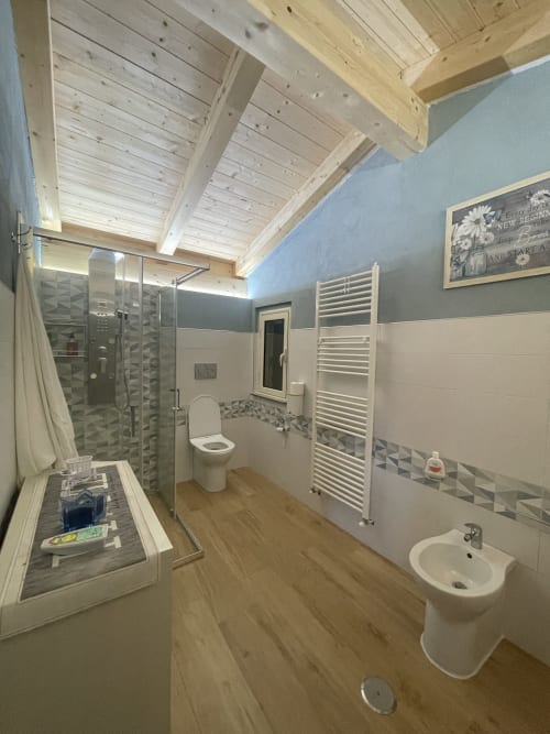 Bagno moderno a Villa Maria con travi in legno, doccia, WC, lavabo, scaldasalviette e dettagli geometrici in piastrelle
