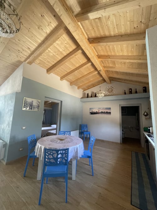 Area aperta con sala da pranzo e living nell'appartamento Villa Maria con soffitto a travi di legno, tavolo rotondo e sedie blu