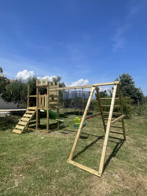 Parco giochi in legno con altalene e struttura da arrampicata nel giardino rurale di Villa Maria, Cosenza