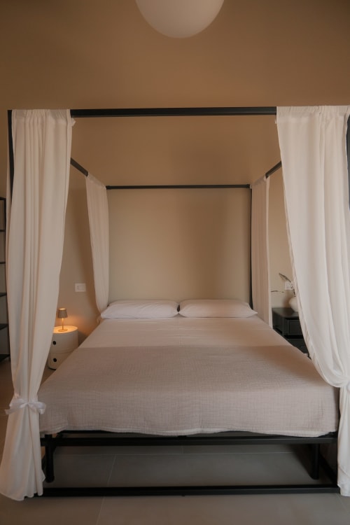 Elegant four-poster canopy bed with sheer white curtains in Nafura hotel's Amira room, Raffadali