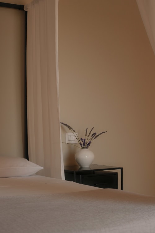 Minimalist hotel room at Nafura with white vase of dried lavender on black nightstand, beige walls and curtains