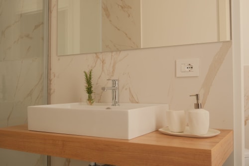 Modern bathroom vanity at Nafura hotel in Agrigento with white vessel sink, wooden counter, and marble backsplash